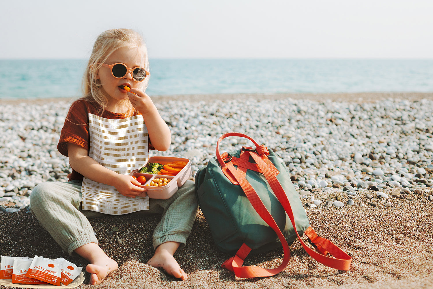 A young girl near a beach eating lunch wearing a NEATsheet with Cinnamon Stick design.