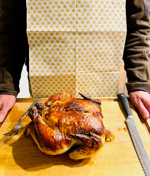 Man serving roast chicken while wearing a NEATsheet - the better alternative to aprons, bibs, and napkins.