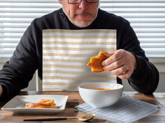 Man eating a grilled cheese sandwich and tomato soup and wearing a NEATsheet with cinnamon stick pattern.