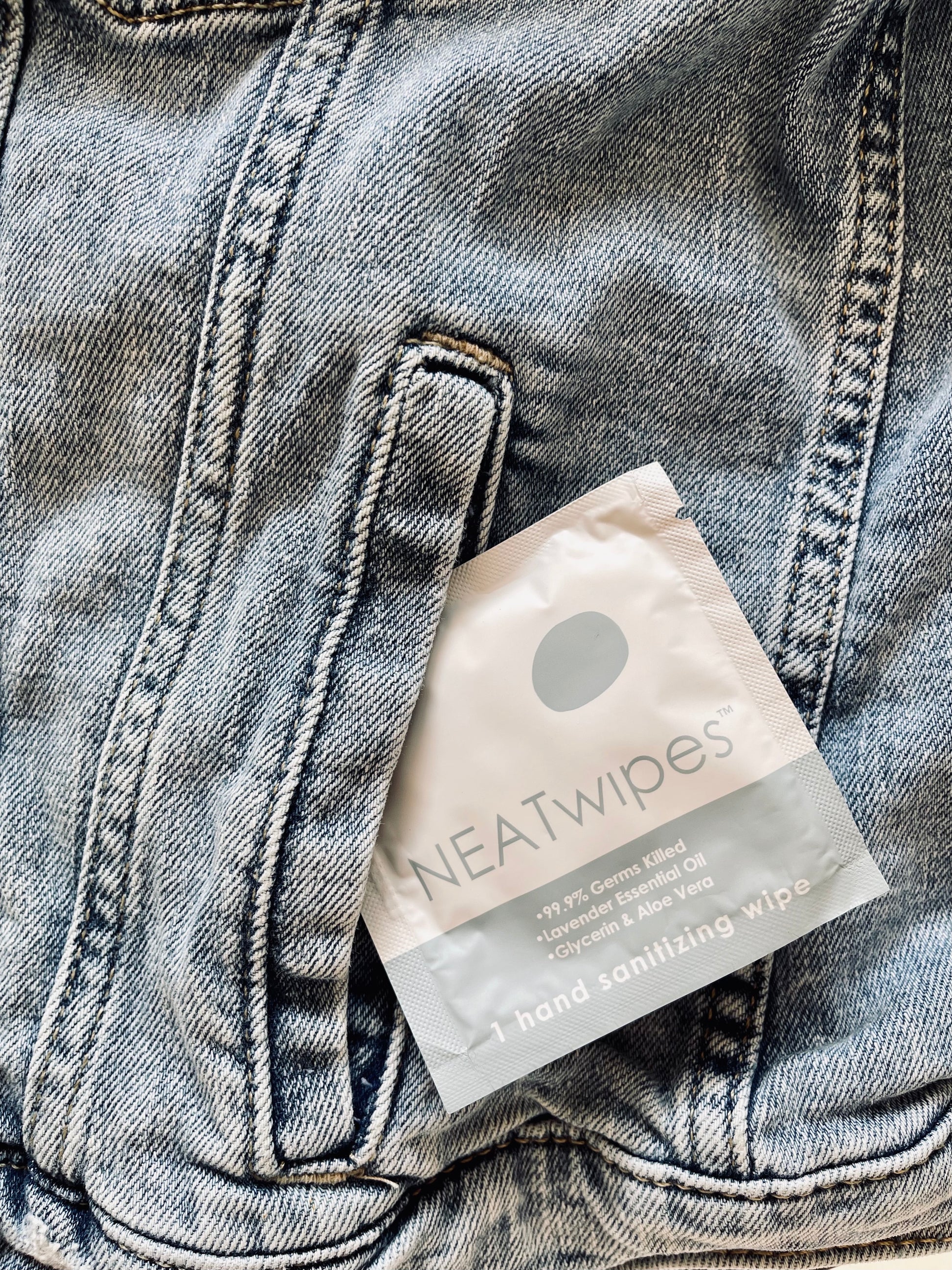 An individually wrapped NEATwipes Lavender hand wipe coming out of a denim jean jacket pocket.